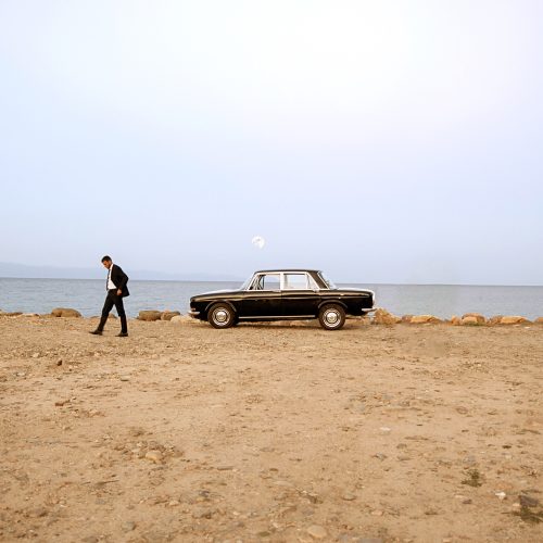 Un uomo in completo scuro si allontana da una vecchia berlina nera, parcheggiata su una spiaggia deserta. Di fronte a lui, solo il mare, la luna e il silenzio.