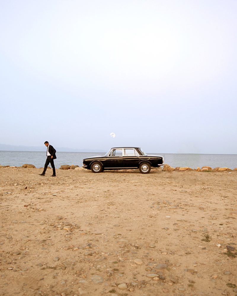 Un uomo in completo scuro si allontana da una vecchia berlina nera, parcheggiata su una spiaggia deserta. Di fronte a lui, solo il mare, la luna e il silenzio.