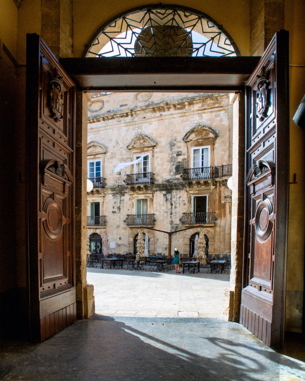 Uno scorcio pieno di luce e fascino senza tempo: le porte aperte del Duomo di Siracusa incorniciano la piazza inondata dal sole, con i suoi palazzi barocchi