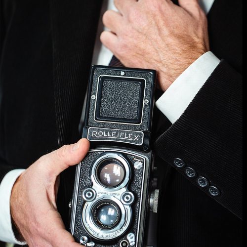 primo piano di una macchina fotografica Rolleiflex, tenuta in mano da un uomo elegante